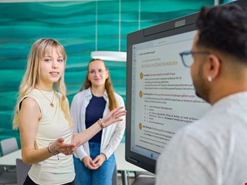 Frau vor Bildschirm junge Frau erklärt etwas vor einem Bildschirm