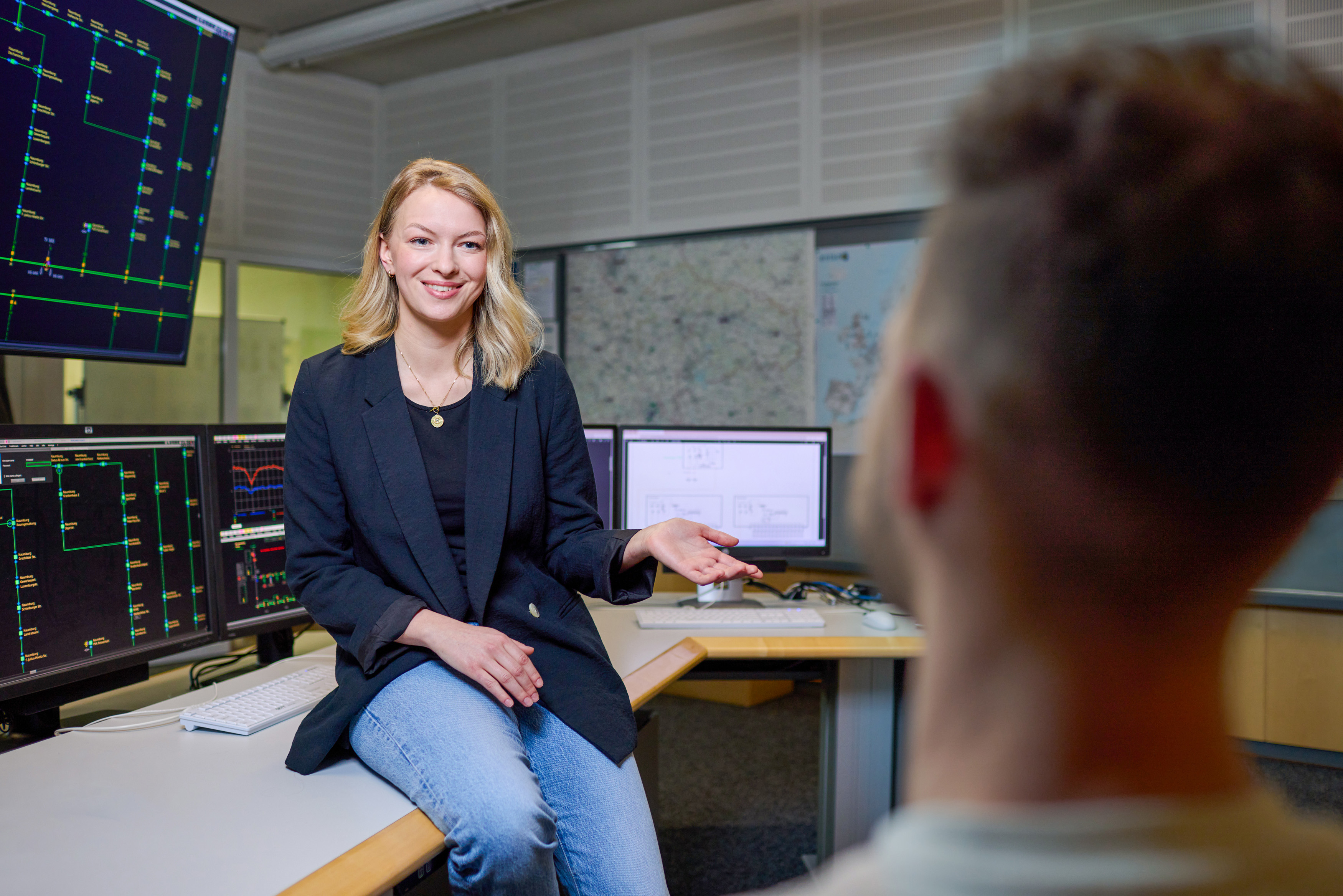 junge Frau sitzt auf der Tischkante und erklärt einem Mann etwas
