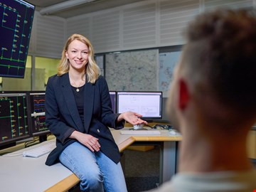 junge-frau-sitzt-auf-tisch junge Frau sitzt auf der Tischkante und erklärt einem Mann etwas