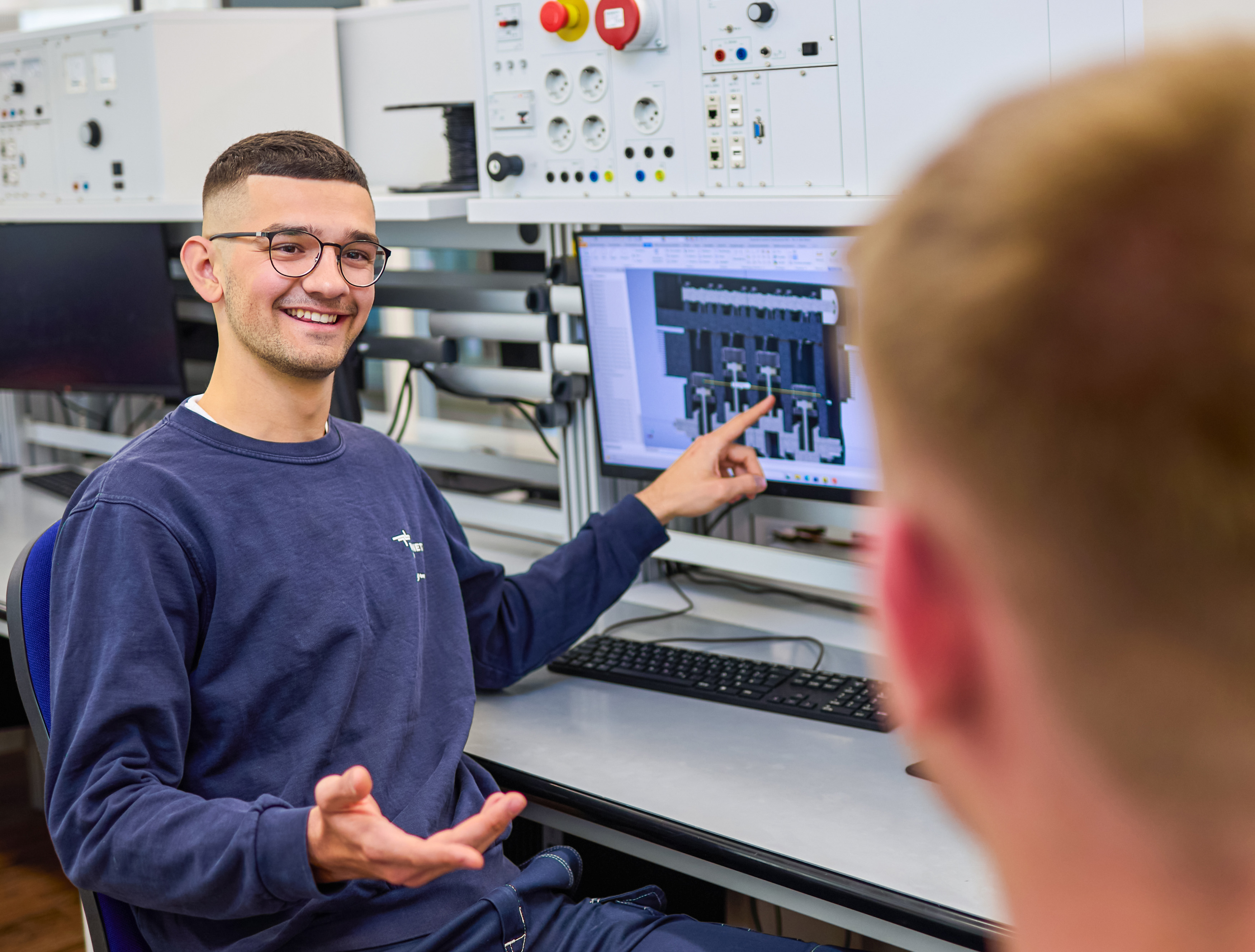 junger Mann erklärte einem anderen Auszubildenden etwas am Monitor