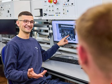 junger-mann-zeigt-auf-monitor junger Mann erklärte einem anderen Auszubildenden etwas am Monitor