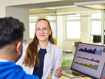 mann-frau-grafiken Mann und Frau im Gespräch am Arbeitsplatz vor zwei Monitoren mit Grafiken
