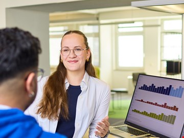 mann-frau-grafiken Mann und Frau im Gespräch am Arbeitsplatz vor zwei Monitoren mit Grafiken