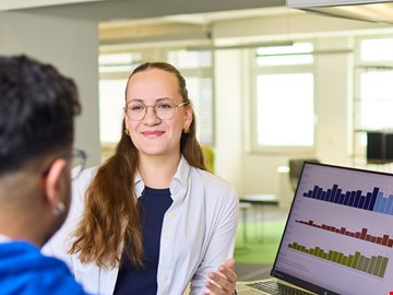 mann-frau-grafiken Mann und Frau im Gespräch am Arbeitsplatz vor zwei Monitoren mit Grafiken