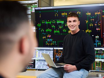 mann-vor-schalttafel junger Mann mit einem Laptop auf dem Schoß sitzt vor einem Screen mit Schaltkreisen